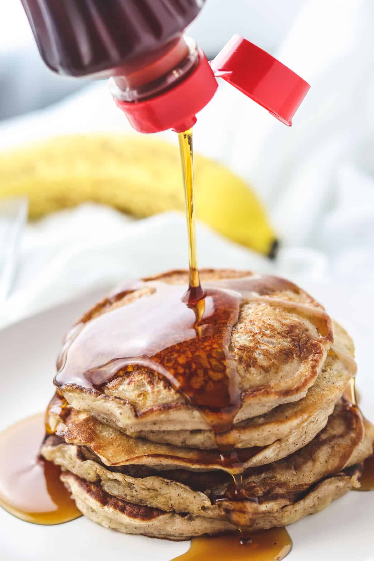pouring syrup on a stack of healthy low calorie pancakes on a white plate
