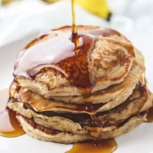 pouring syrup on a stack of pancakes