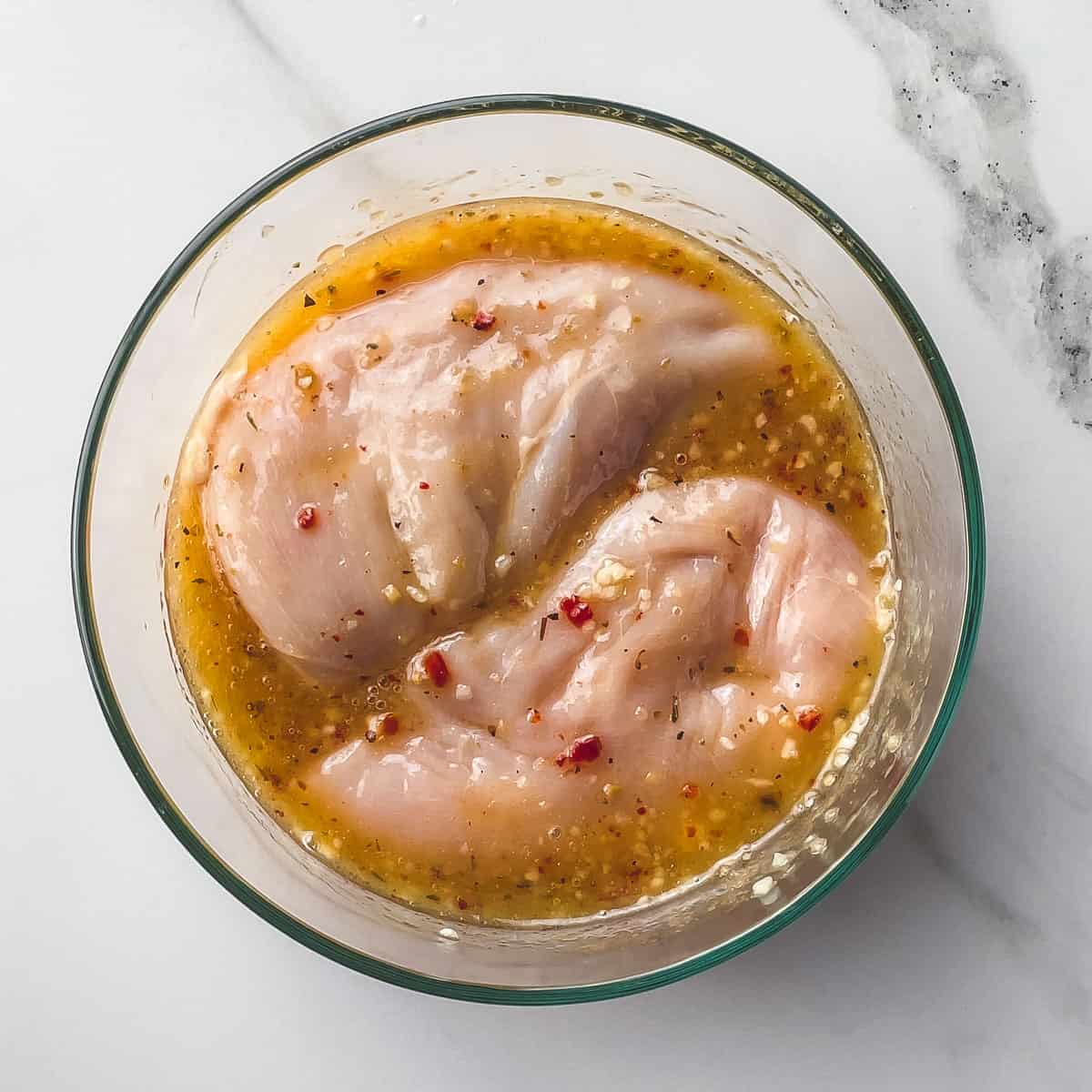 chicken breasts marinating in Italian dressing and garlic in a bowl