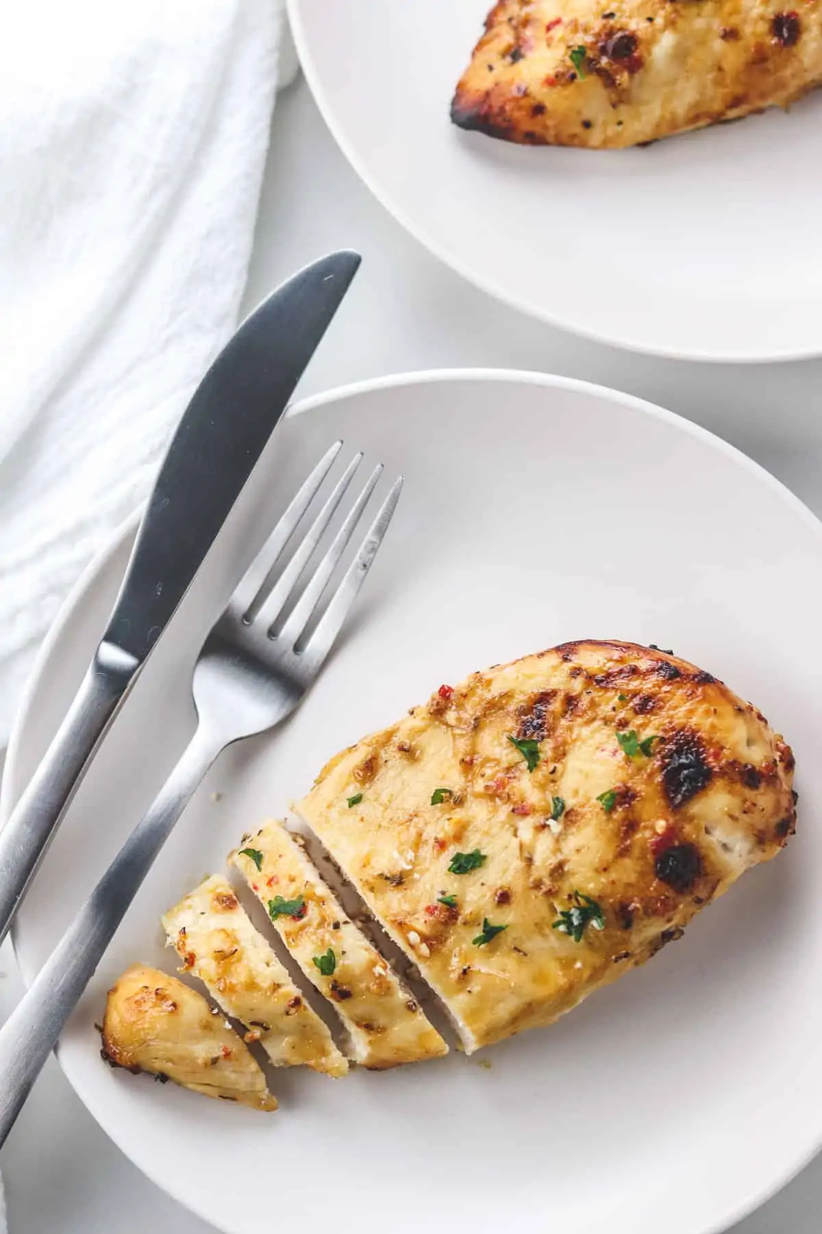 cut chicken breast on a white plate with a fork and knife