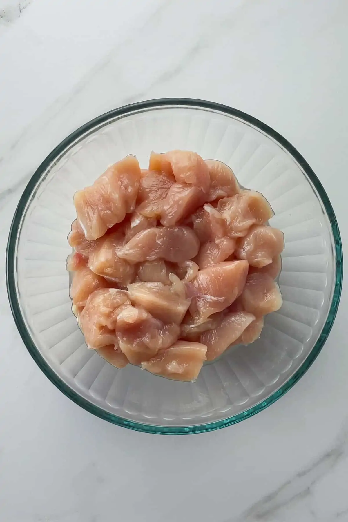 raw chicken pieces in a glass mixing bowl