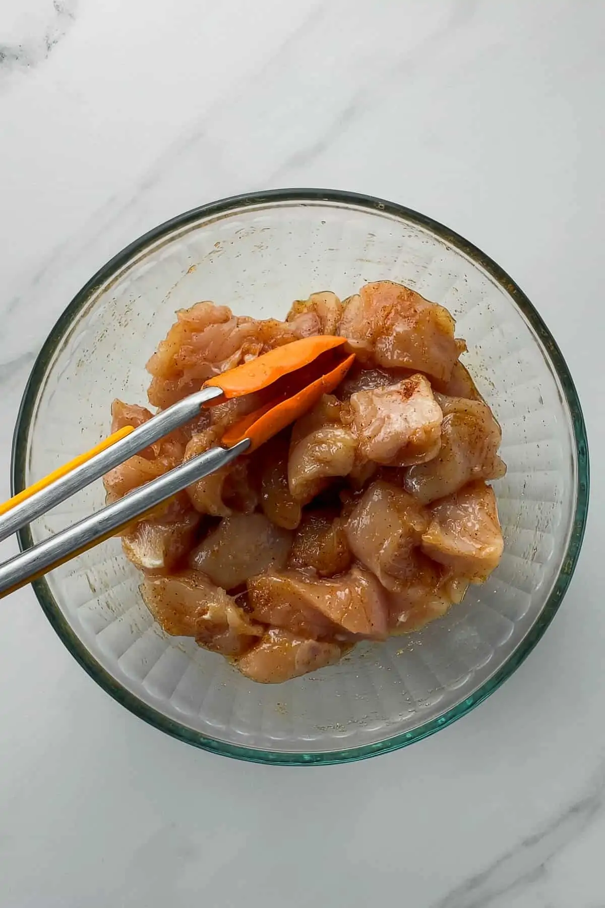 raw chicken mixed with rotisserie seasonings in a glass mixing bowl