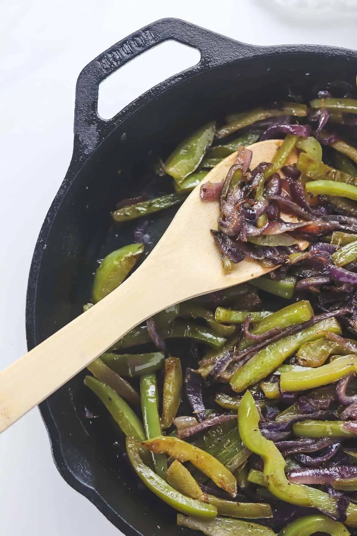 fajita peppers and onions in a cast iron skillet with a wooden spoon