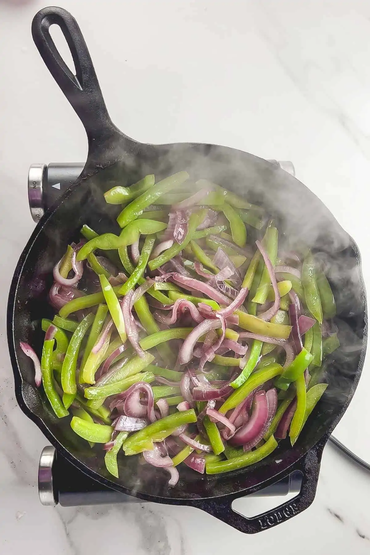 peppers and onions cooking in a cast iron skillet