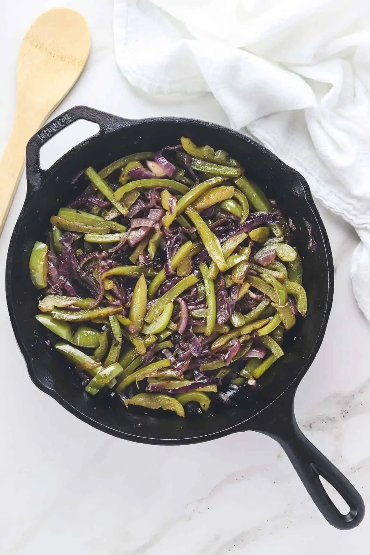 fajita peppers and onions in a cast iron skillet with wooden spoon