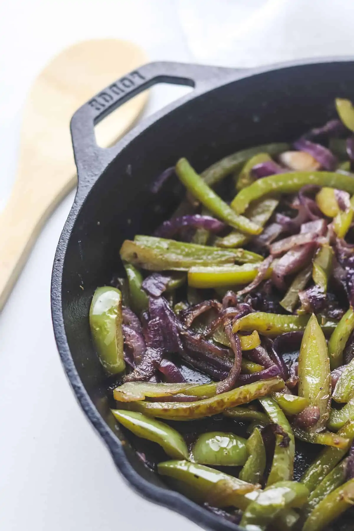 fajita veggies in a cast iron skillet with a wooden spoon