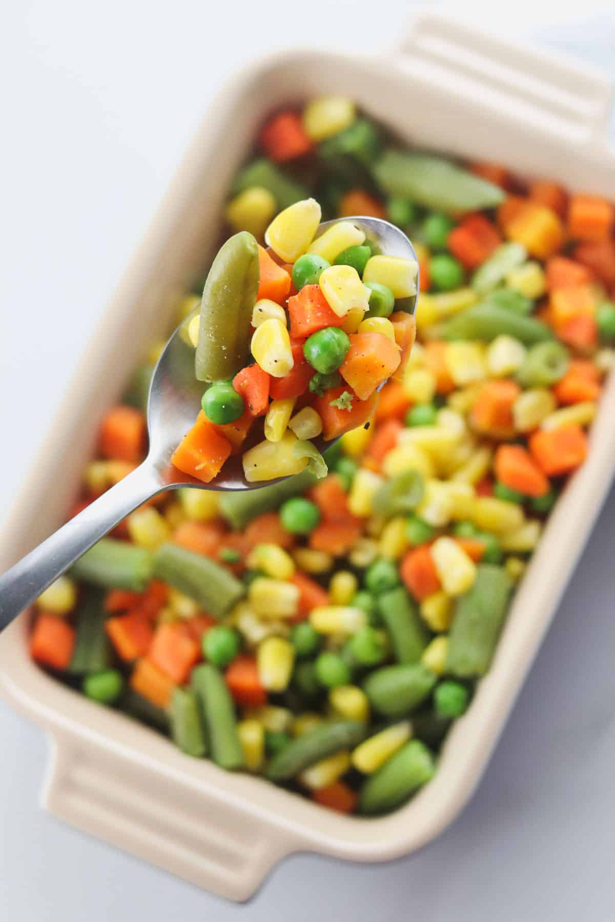 scooping a spoonful of mixed vegetables including corn, green beans, carrots, and peas
